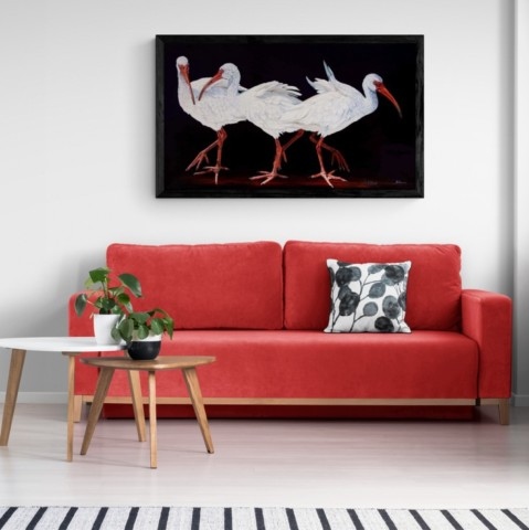 “Painting of white ibises displayed in a living‑room setting above a red sofa by wildlife artist Laurence Saunois.
